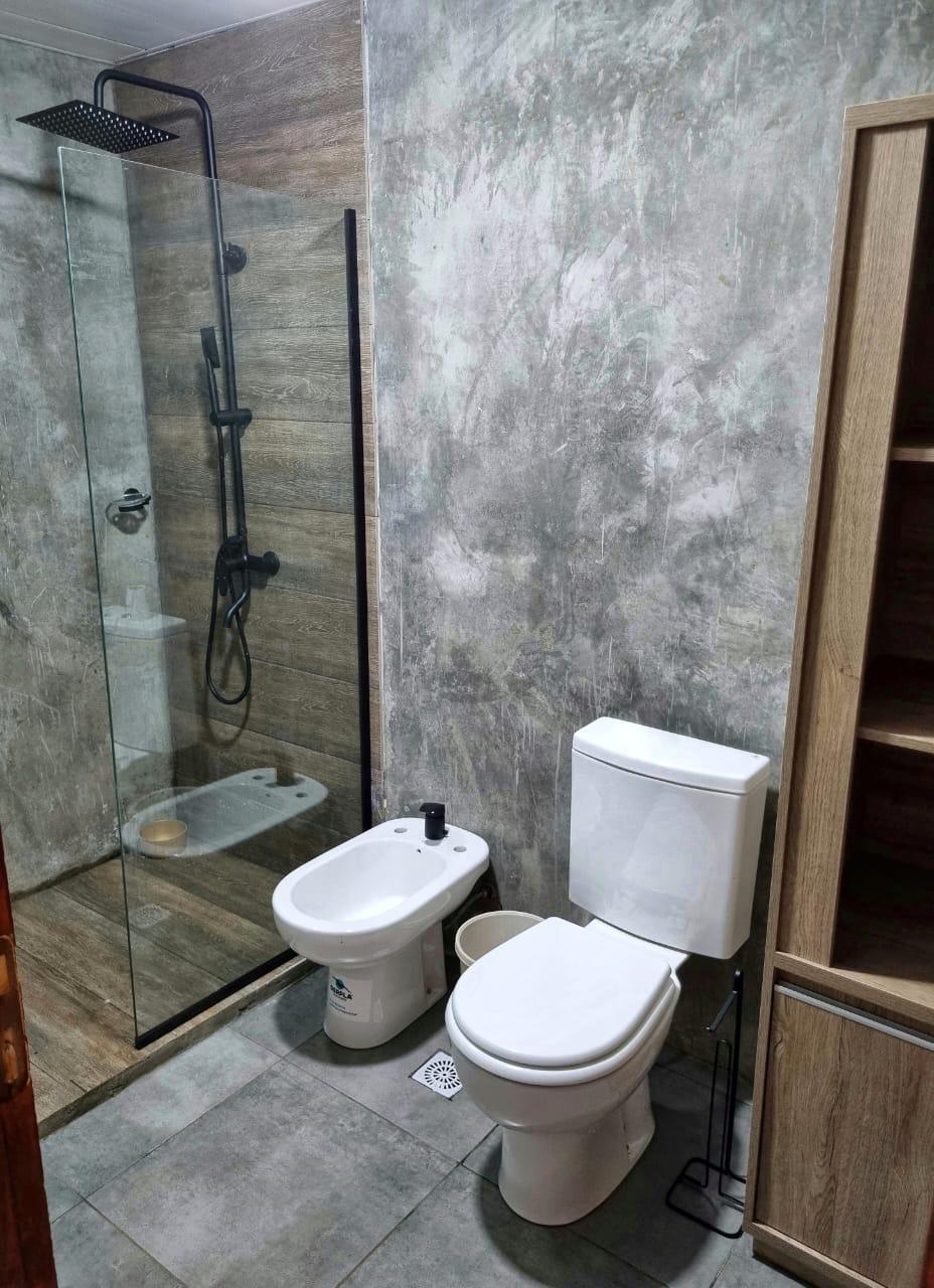 Baño con ducha de mampara y paredes de cemento alisado